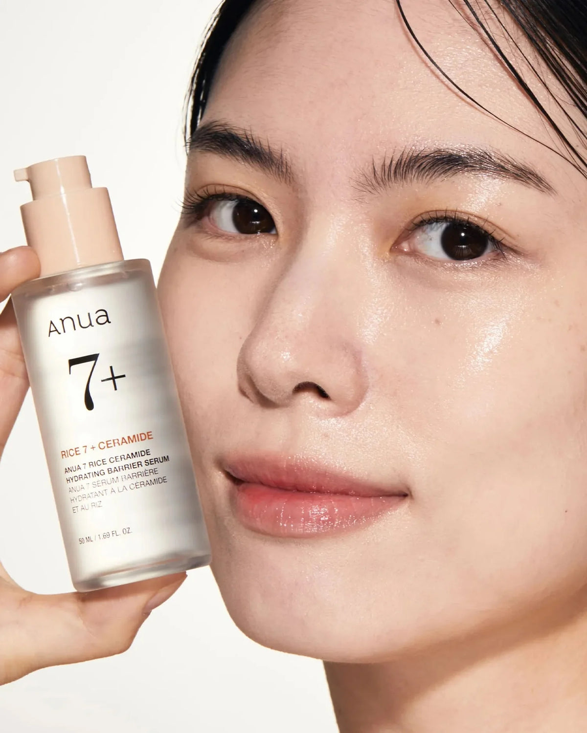 Kvinde med glansfuld hud holder Anua Rice 7 Ceramide Hydrating Barrier Serum 50ml tæt ved ansigtet.