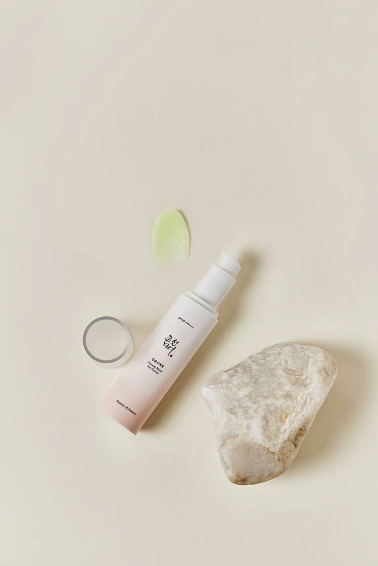 Flaske Beauty of Joseon Ginseng Moist Sun Serum 50ml på beige baggrund med lys sten og grøn geltekstur.