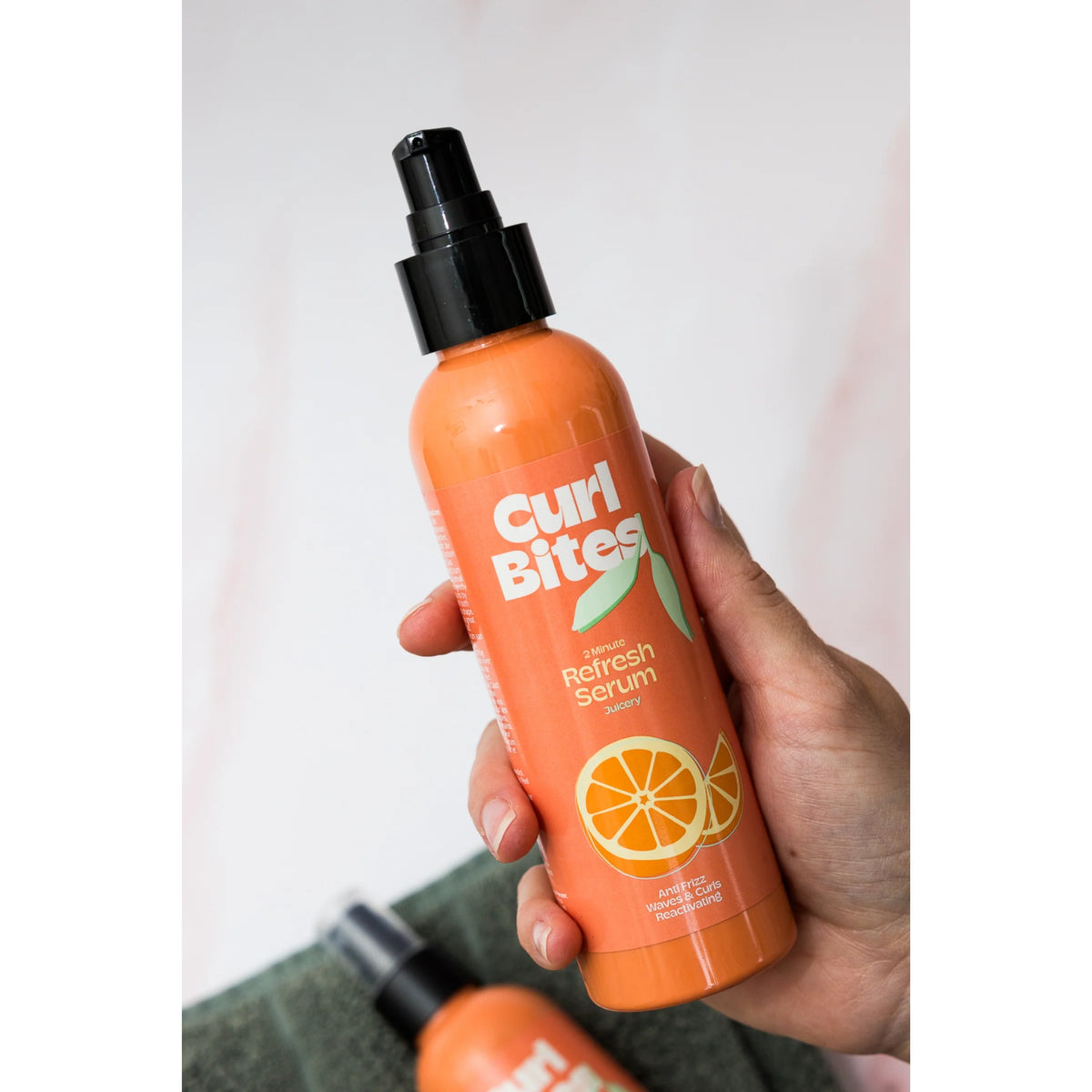 Hånd holder Curl Bites 2 Minute Refresh Serum, orange flaske med pumpe og appelsinmotiv.