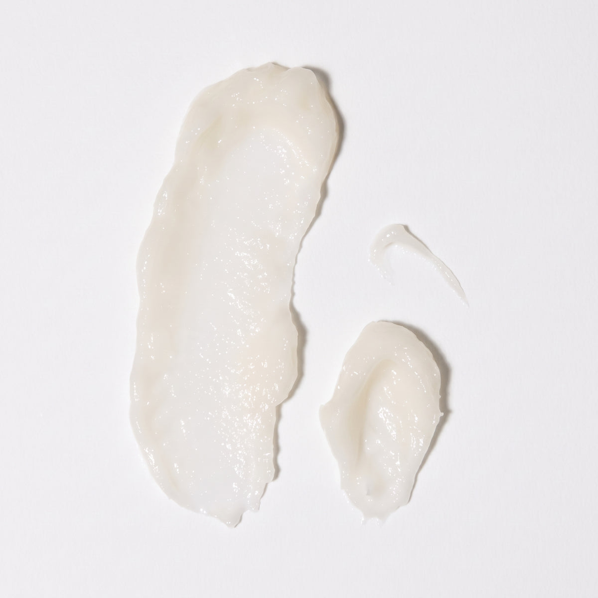 Cremet hvid hudplejecreme i tre swatches på lys baggrund, viser tekstur og glans.