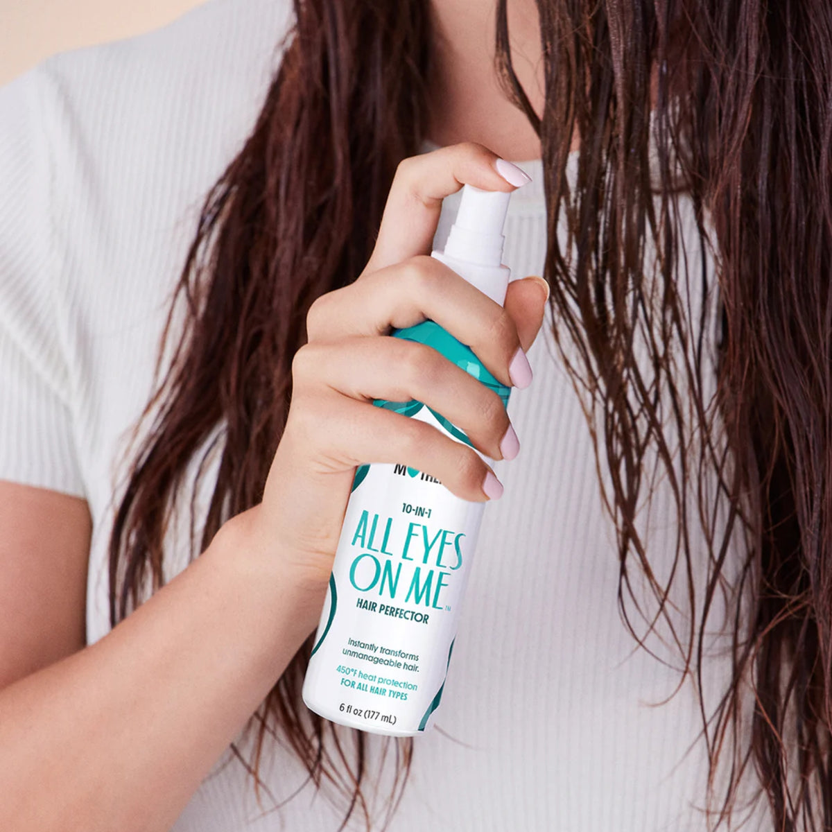 Kvinde med langt vådt brunt hår sprayer All Eyes On Me Hair Perfector varmebeskyttelse i håret.