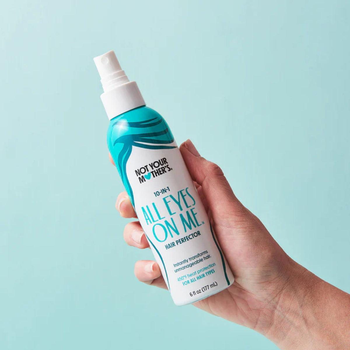 Hånd holder Not Your Mother's All Eyes On Me 10-i-1 hair perfector spray mod lyseblå baggrund.